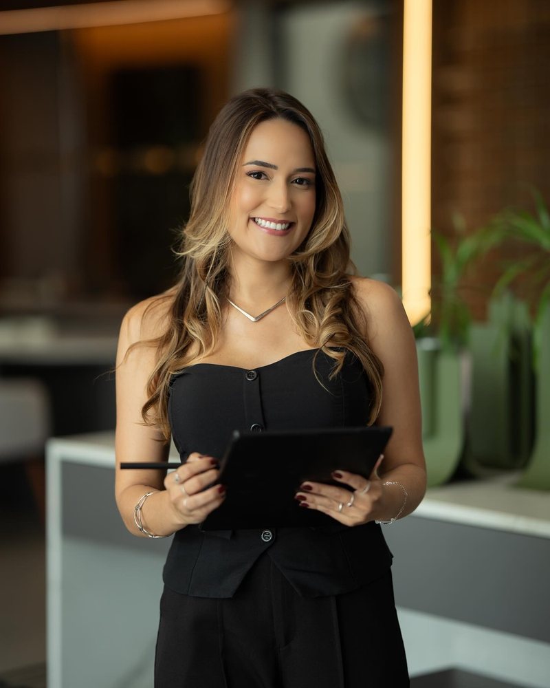 Maria Madalena segurando um tablet, em pé no escritório